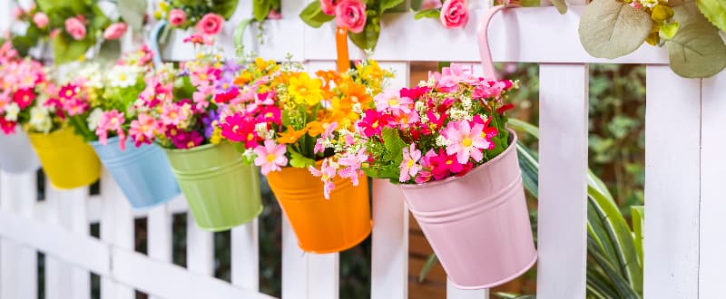 colourful flower pots/tins hanging along a white picket fence