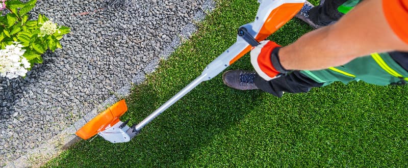 A person uses a string trimmer to neatly cut grass edges along a path in a well-maintained garden.