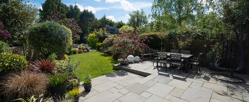 Spacious landscaped garden featuring a paved patio, outdoor dining area, lawn and mature planting, demonstrating effective use of space in a large garden design.